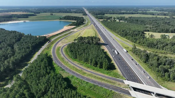 A aerial photo showing new highway roads amid a verdant and lush backdrop with some water in the background.