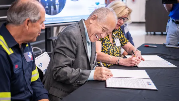 Houston ISD Superintendent Mike Miles smiles while holding a pen to sign a document