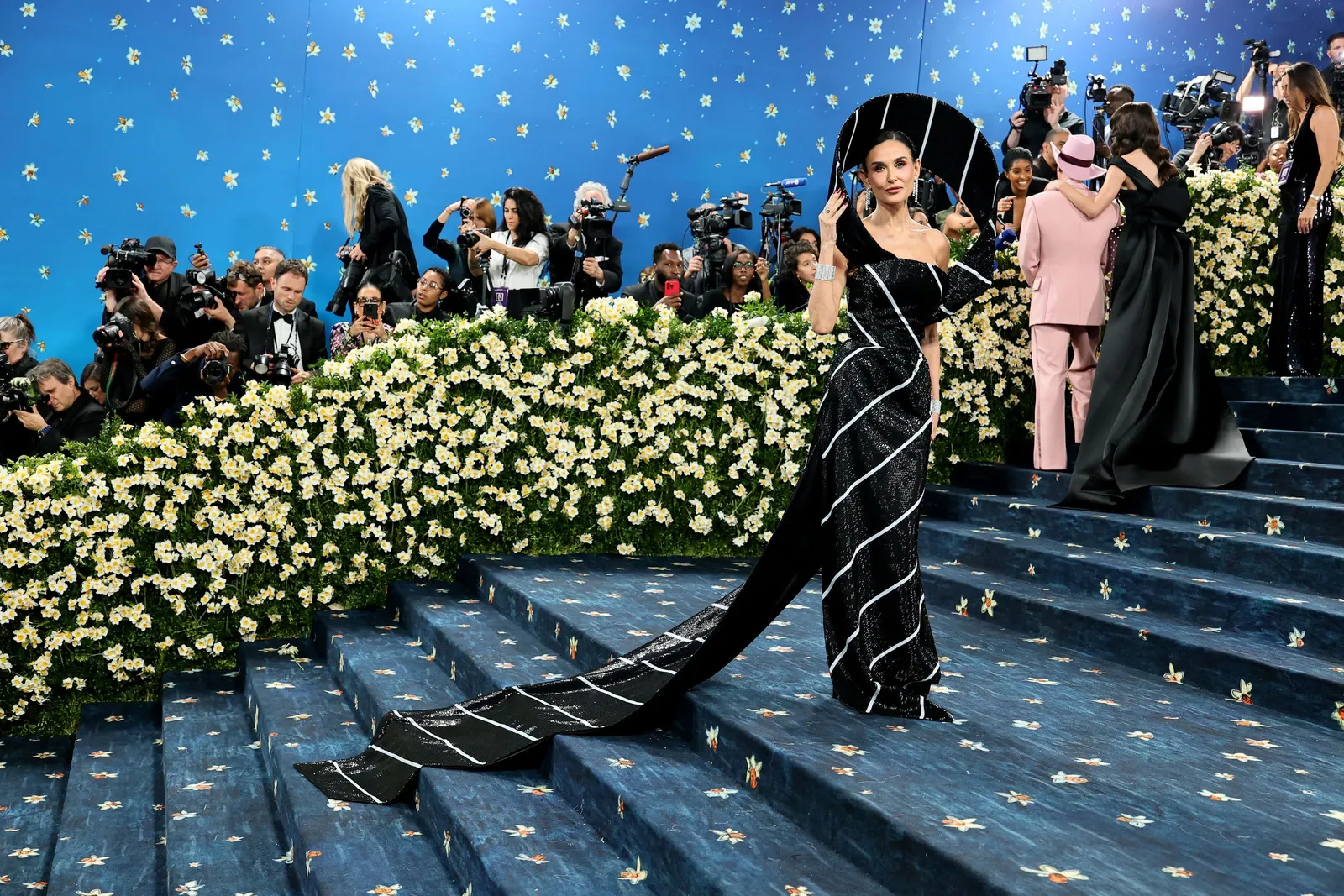 A woman in a black and white striped dress with a long tail poses on a blue staircase.