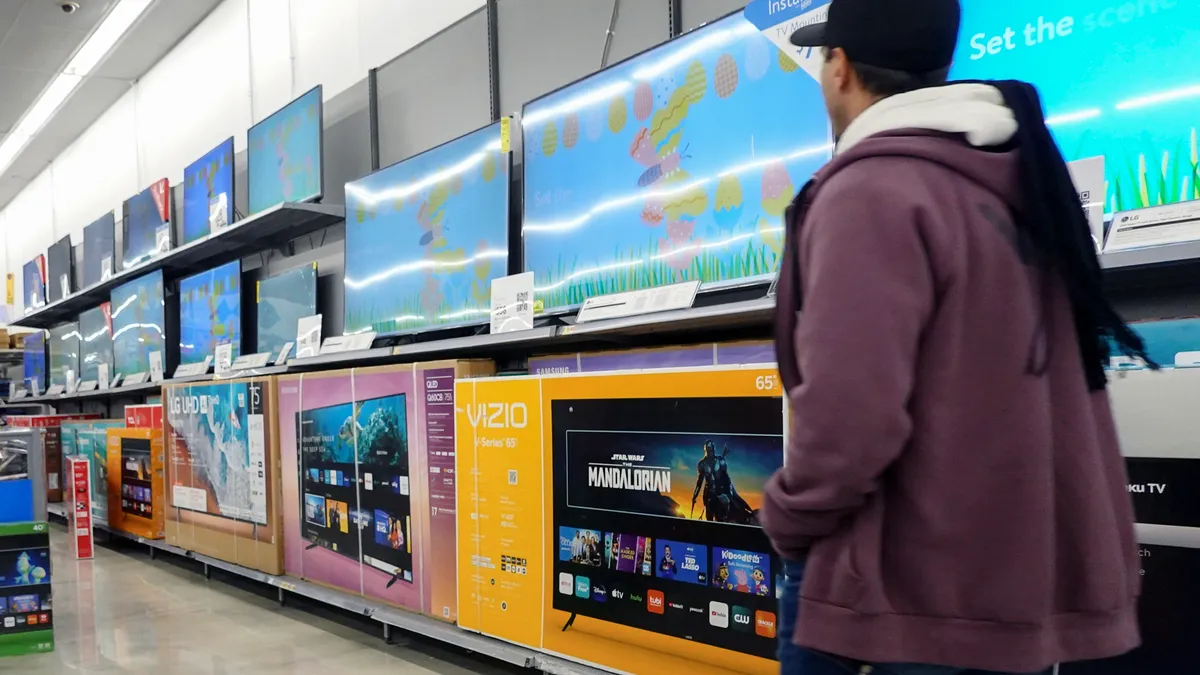 A customer walking down an aisle at Walmart with TVs on shelves.