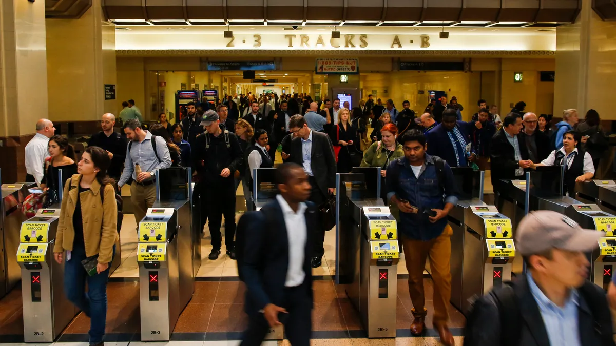 Crowd of people walking through turnstiles at a train station.