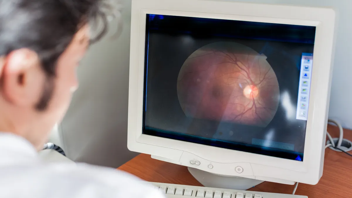 A stock image of an ophthalmologist looking at a retina scan on a computer monitor.