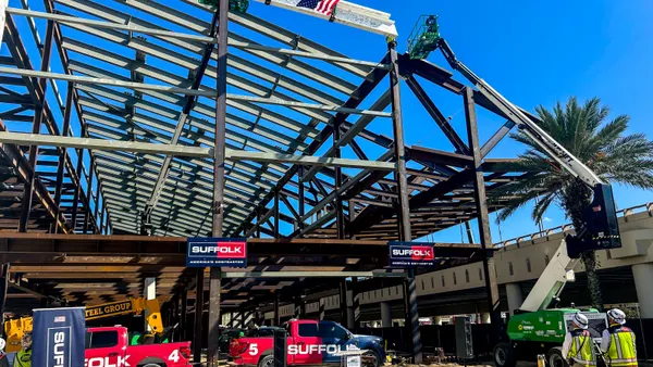 A steel frame of a building under a blue sky on gravel is in the foreground.