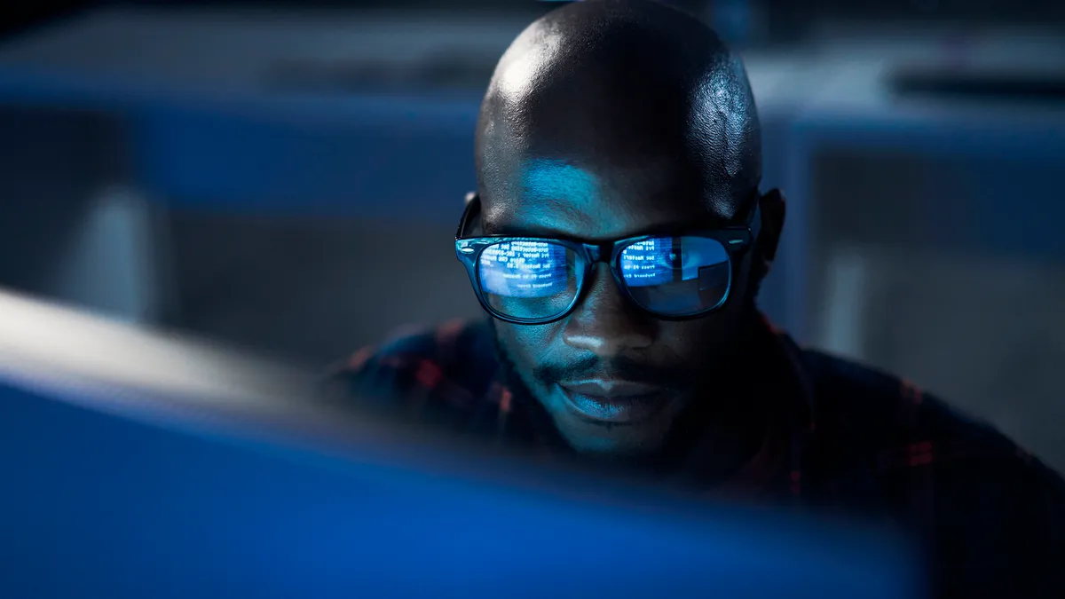 a close up of a technology worker wearing glasses, looking into a computer screen showing code