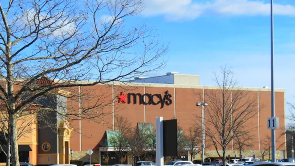 A tree with bare branches sits to the left of a mall store, with a blue sky above.