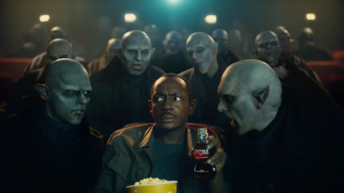 A person holds a bottle of Pom Wonderful surrounded by vampires in a movie theater