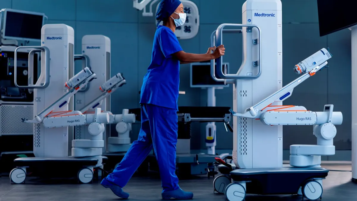 A clinician uses handles to push a robotic system component on wheels.