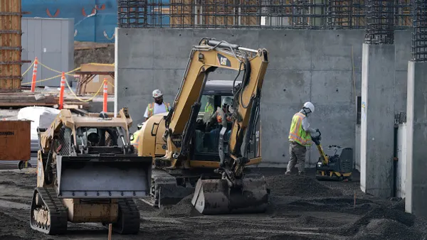 A group of construction workers labor around heavy equipment and vehicles.