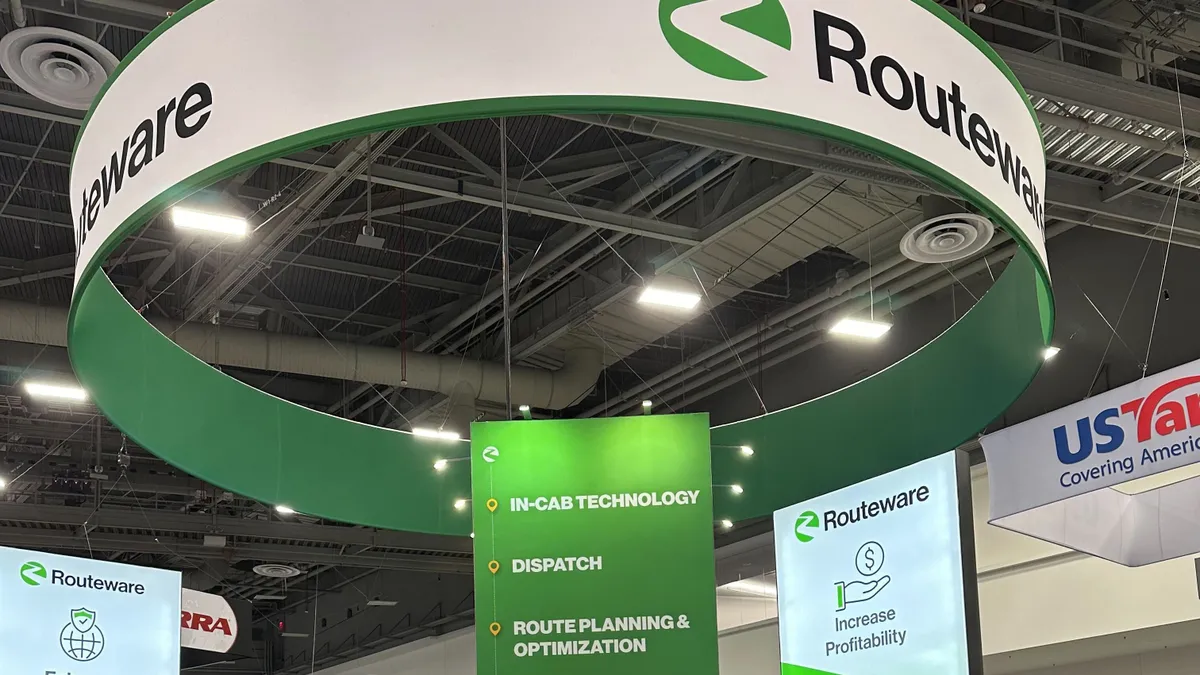 A circular sign hanging above a booth at a trade show reads "Routeware."