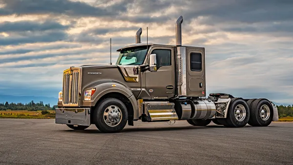 A freight truck parked on a paved road with a nice cloudy backdrop.