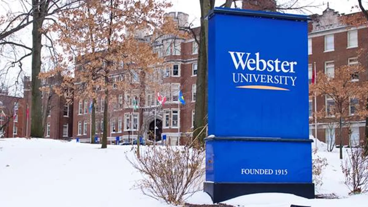 A snow covered landscape, with a sign at the far right of the frame advertising for Webster University.