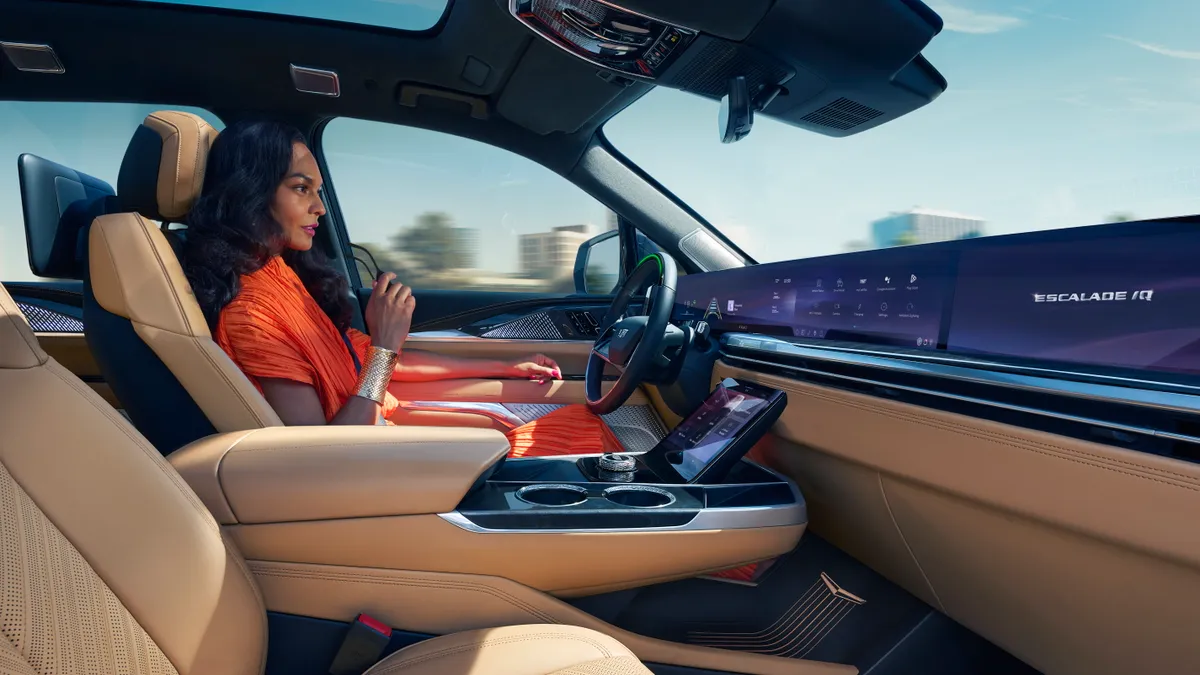 A woman behind the wheel of a Cadillac Escalade IQ with a pillar-to-pillar dashboard display in view.