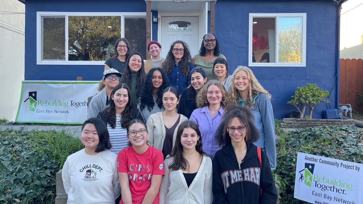 A group of girls and women pose for a photo in front of a home.