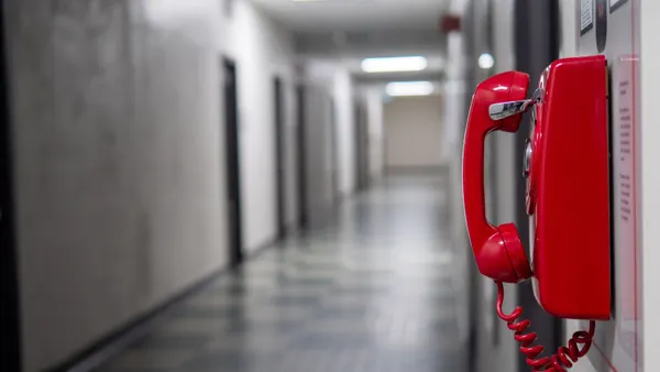A red telephone hangs on the wall in a hallway.