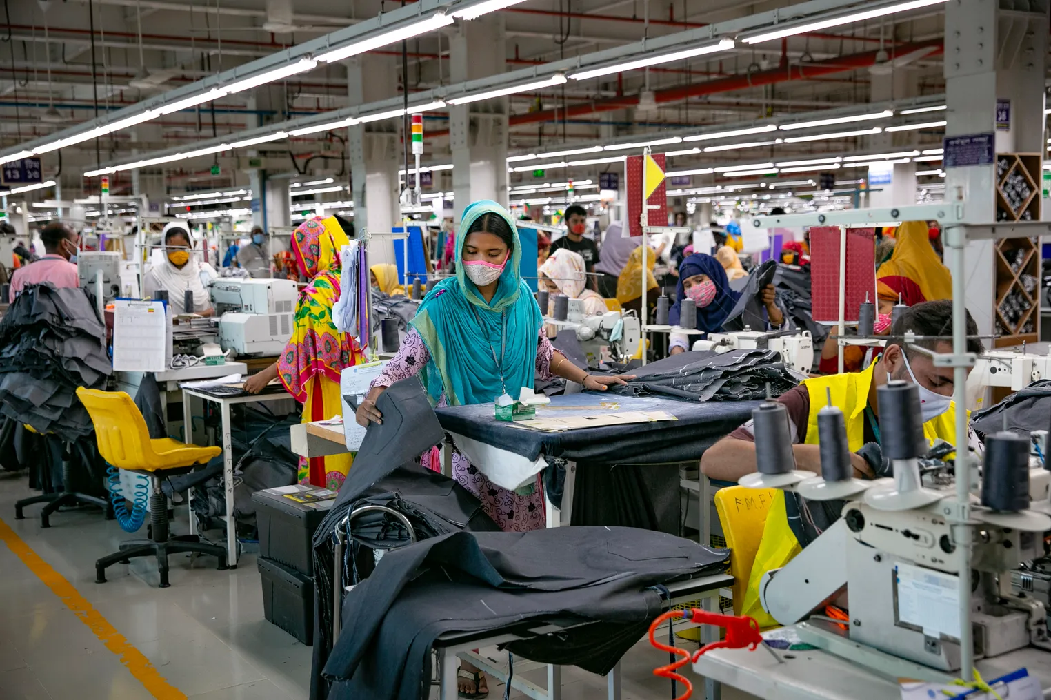 A factory with rows of Bangladeshi garment workers behind their sewing machines working on fashion garments