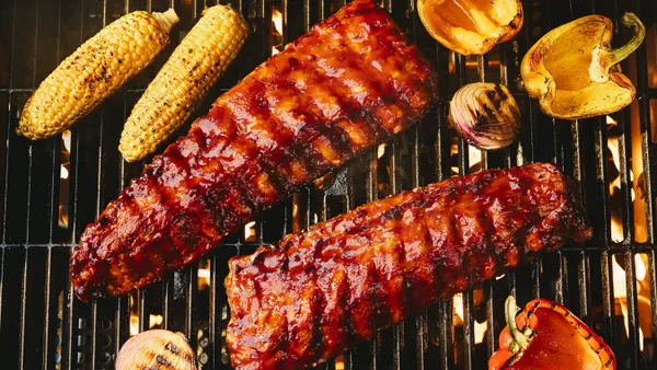 A pair of glazed pork ribs sit on a blazing charcoal grill.