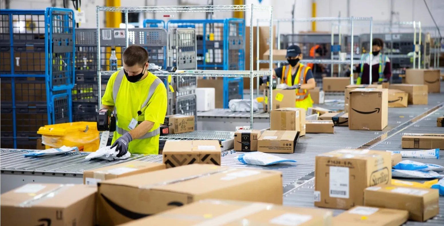 Three Amazon workers in a warehouse prepare orders.