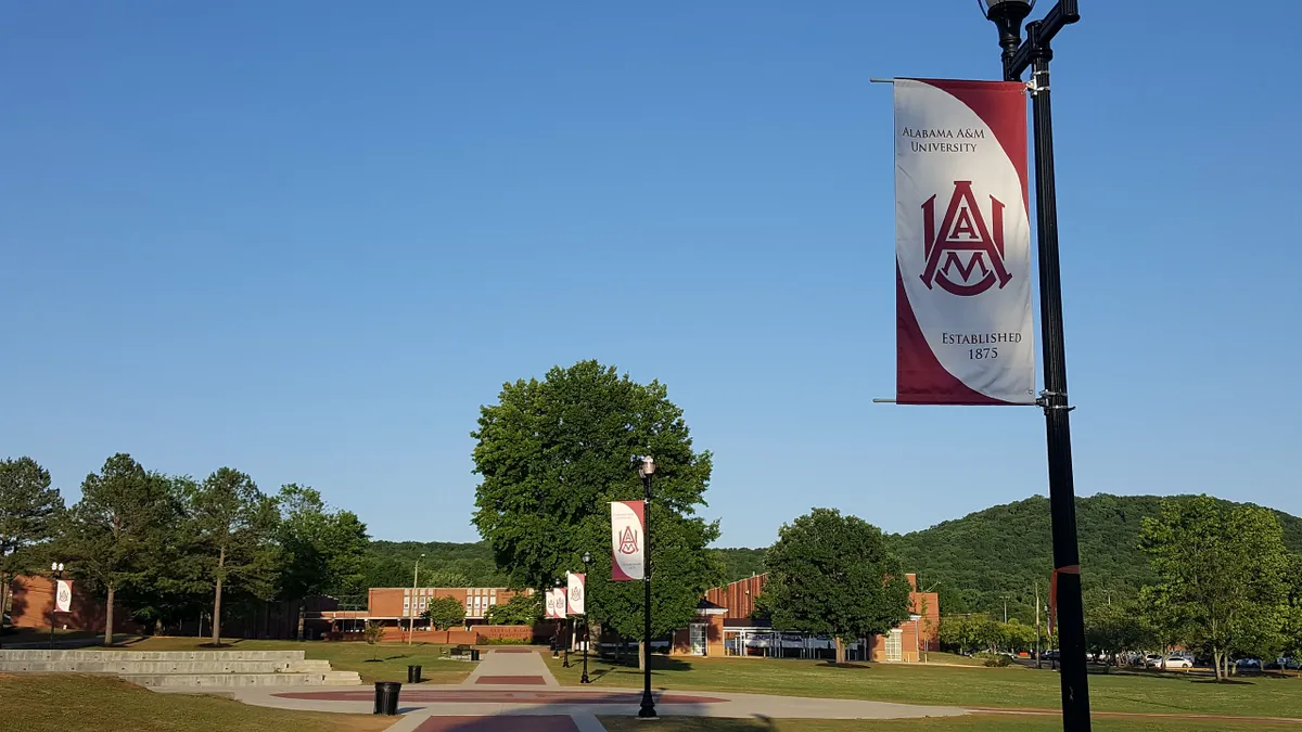 In a general view of a walkway on the campus of Alabama Agricultural and Mechanical University in Hunstville, Alabama, a lamp post displaying a sign of the university's name and logo is in the foreground.