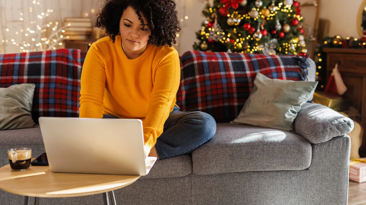 A woman shops on her computer in front of a Christmas tree.