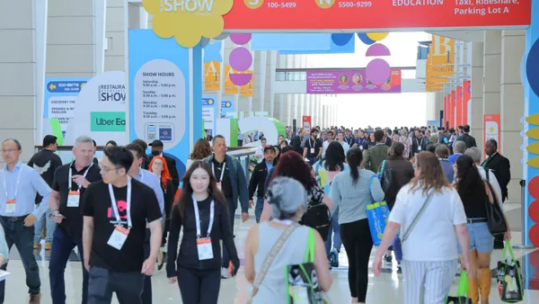 A potograph of a group of people walking through a convention hallway. Signs say National Restuanat Association Show