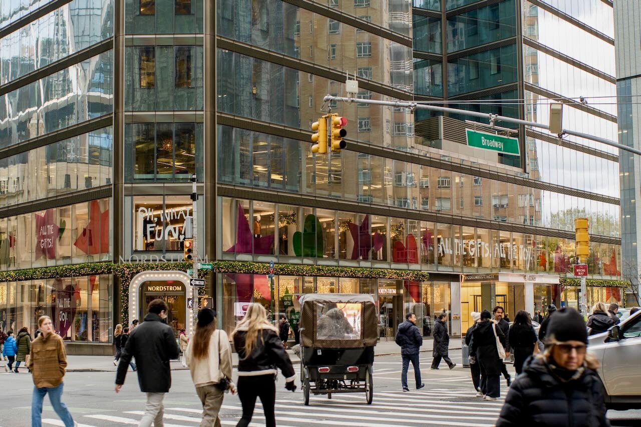 People walking around a city, a buggy in the middle of the intersection.