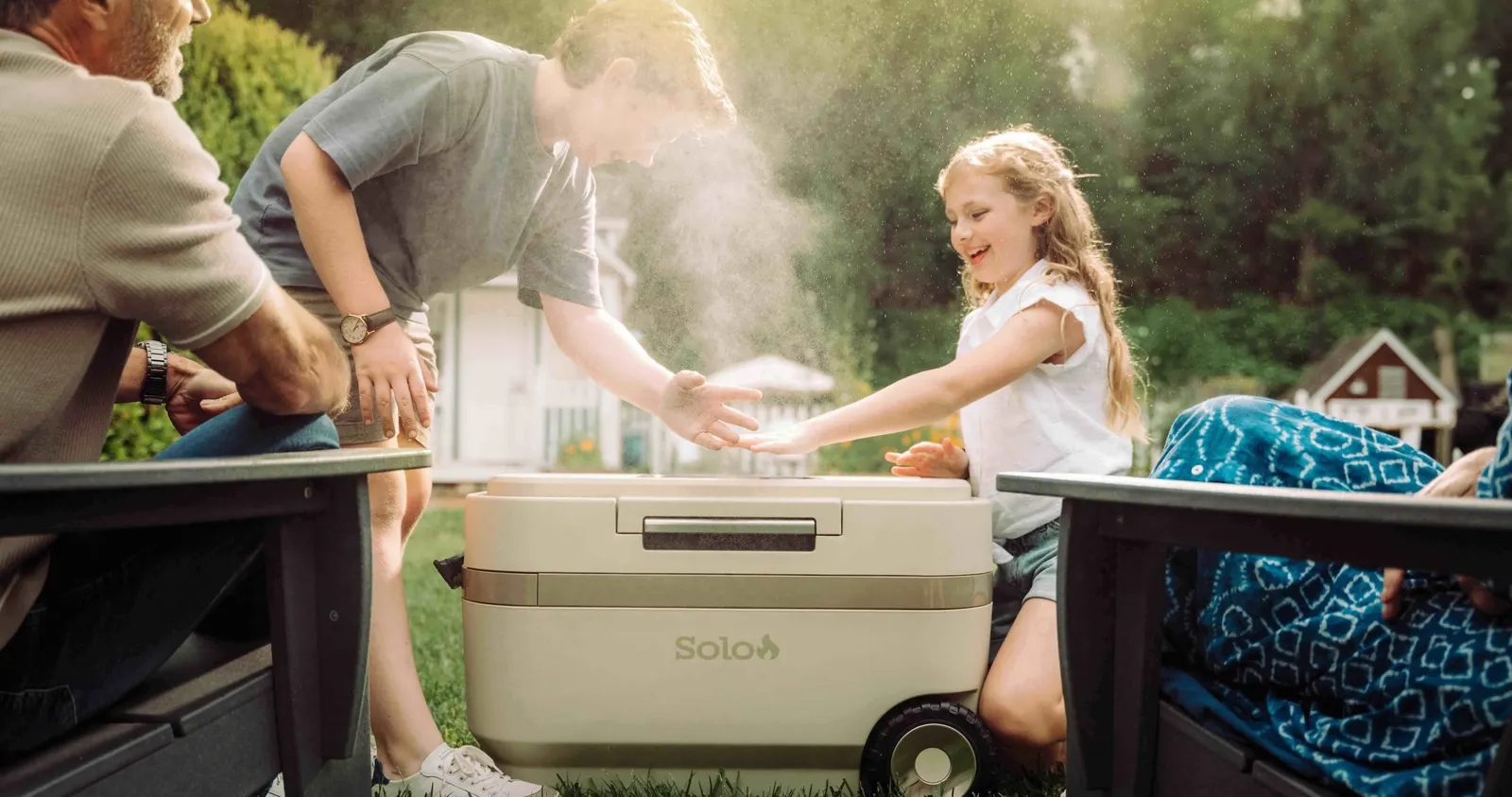 People gather around a tan cooler in the grass.