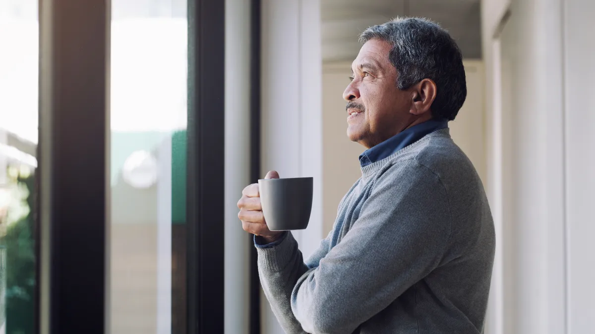 Man smiles while holding a mug and looking out the window.