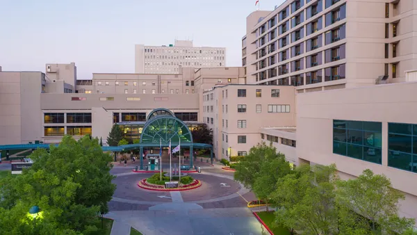 A shot of a large medical center's entrance from a second-story view, including a tree-lined street and glass-faced archway.