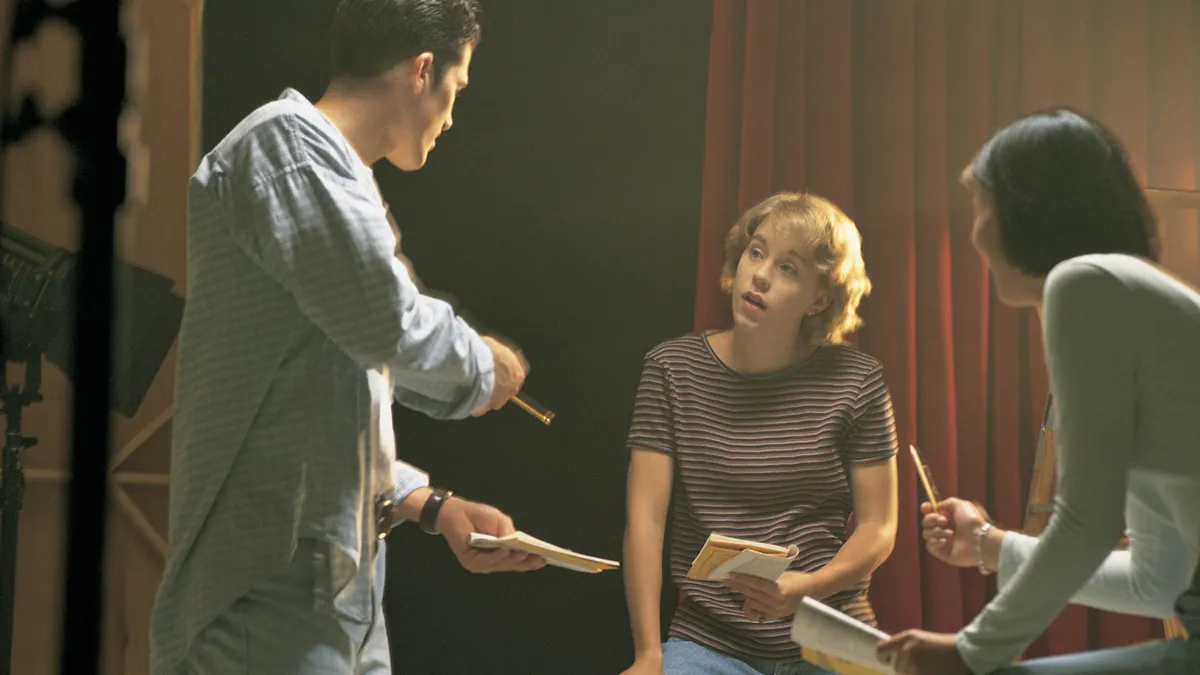 Three high school theater students share notes on a performing arts center stage.