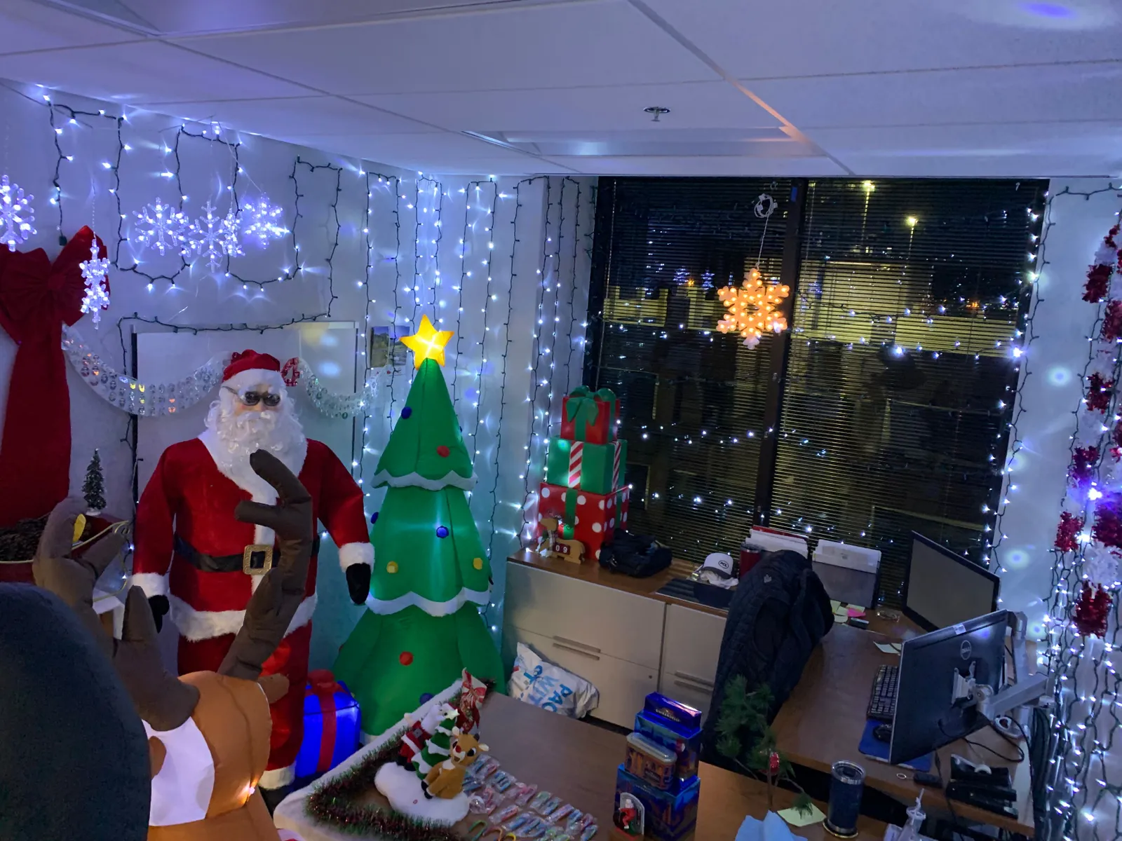 An office with Santa Claus in sunglasses, a Christmas tree and holiday lights adorning the walls.