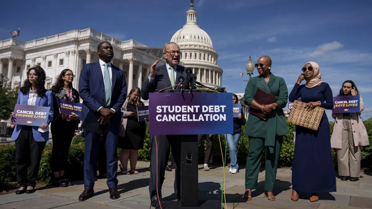 Senate Majority Leader Chuck Schumer stands behind a podium with a sign reading "student debt cancellation."