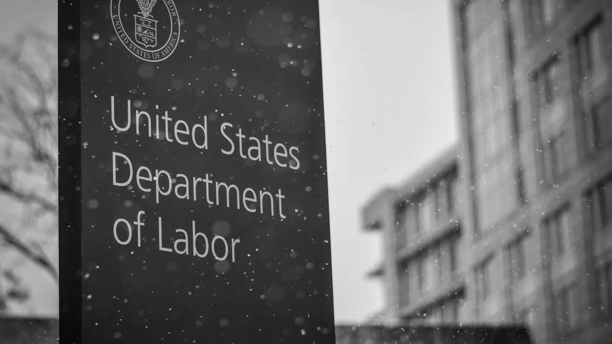 A black and white photograph of the US Department of Labor's sign, with its insignia.