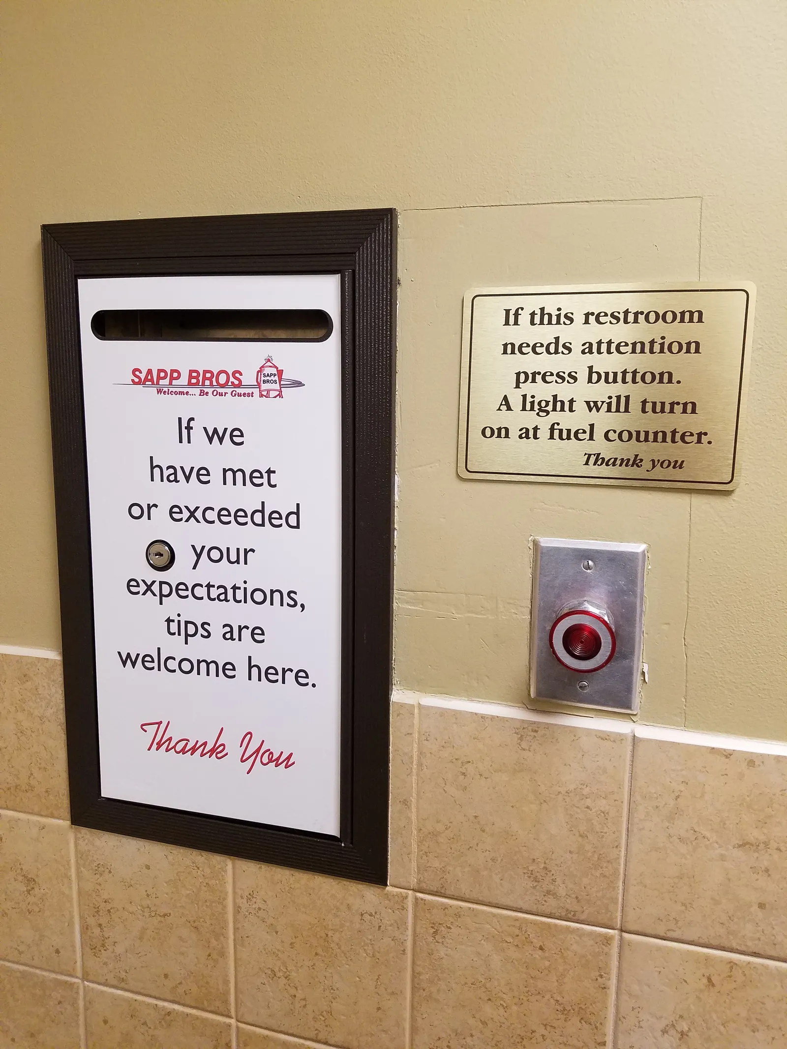 A photo of a sign inside a restroom. The sign reads &quot;If we have met or exceeded your expectations, tips are welcome here.&quot; Another sign above a button reads &quot;If this restroom needs attention press button. A light will turn on at the fuel counter.&quot;