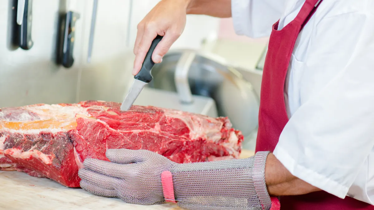 Butcher wearing a glove whilst preparing cut of beef