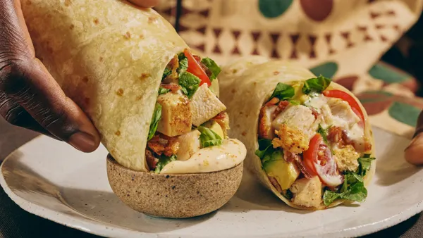 A hand holds a wrap and dips it into a cup of sauce.