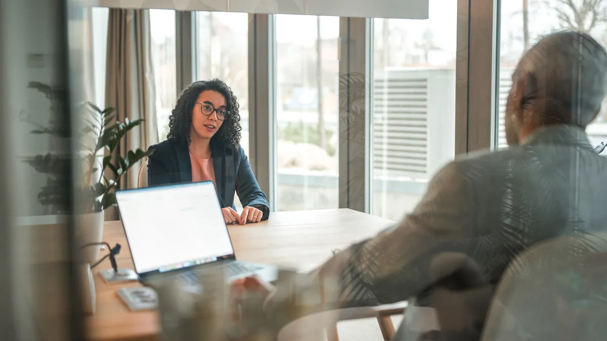 An job interviewer speaks to a candidate across the desk from her in a well-lit office