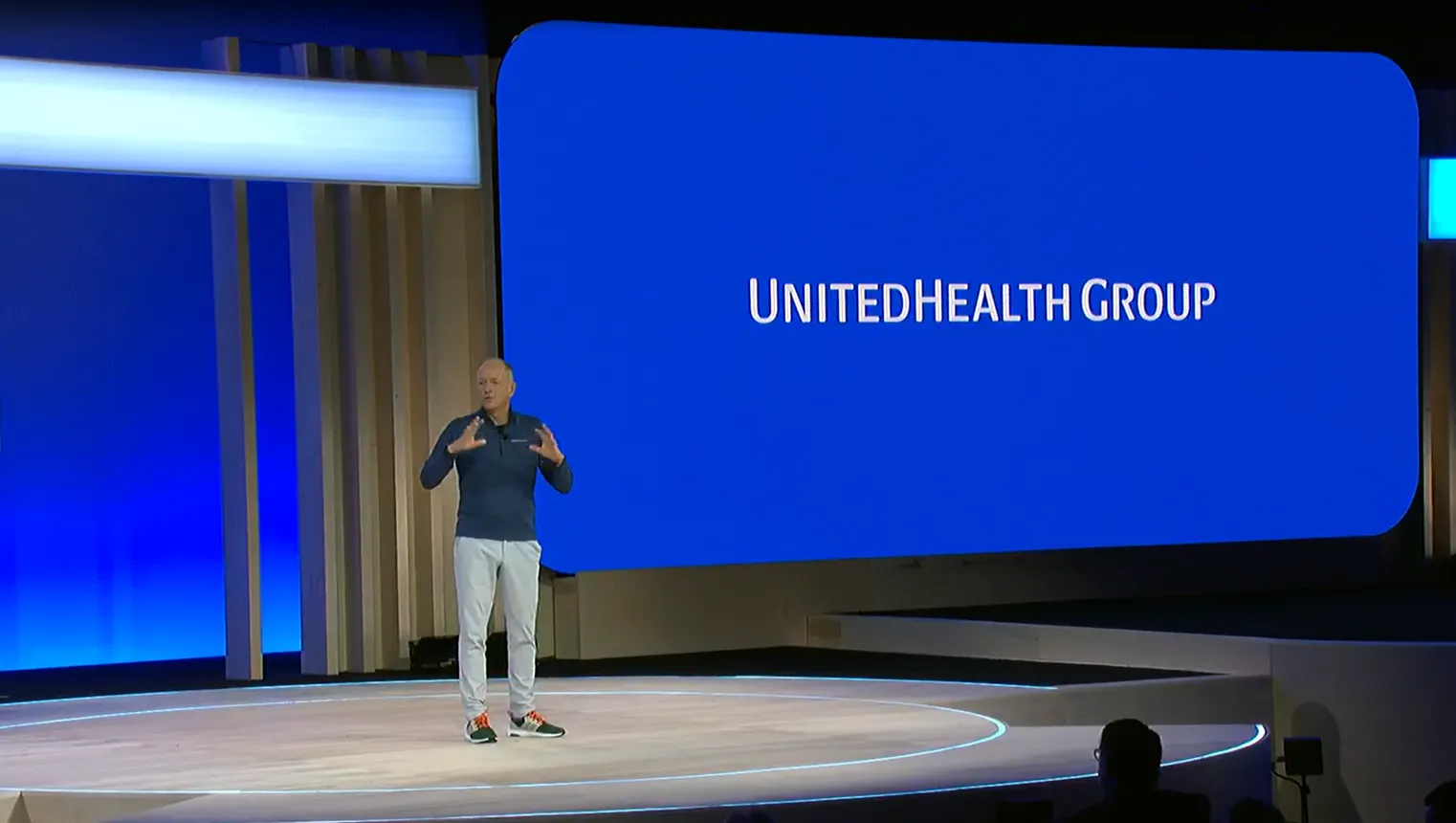 UnitedHealth CEO Andrew Witty speaks onstage behind a screen projecting the UnitedHealth logo.