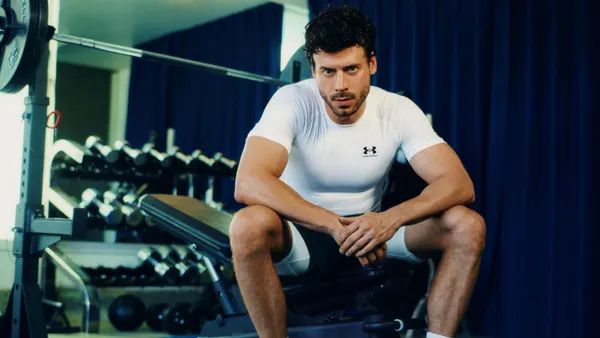 A person in Under Armour clothing sits on a bench press in a gym.