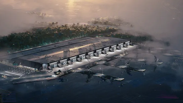 A large, gunmetal-gray building with 10 doors numbered, with a shipyard and water in front of it.