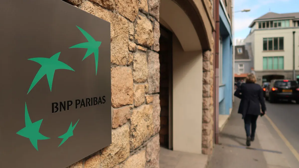 "BNP Paribas" is seen on a sign on a building as a person walks by in the background.