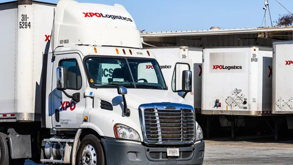 An XPO semi-truck with trailers in the background at a site.