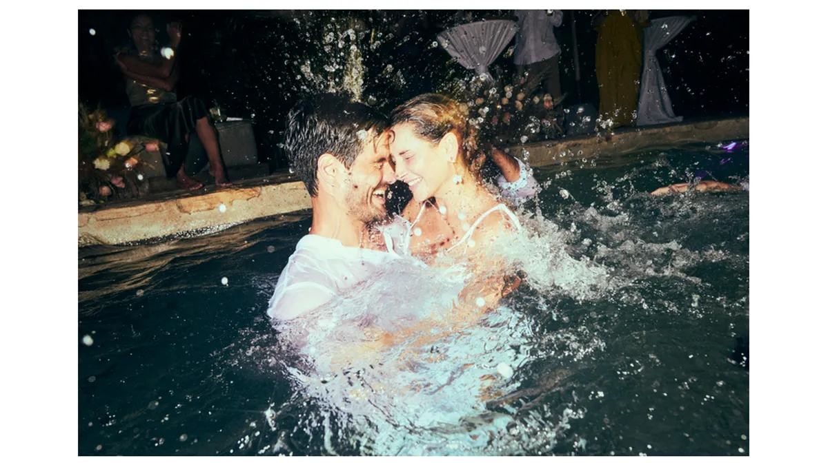 Two people wearing white embrace in a pool in the night.