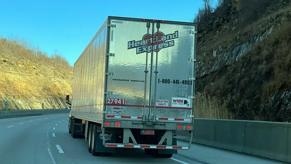 A tractor and trailer bearing the Heartland Express brand drives down a hill on an interstate.