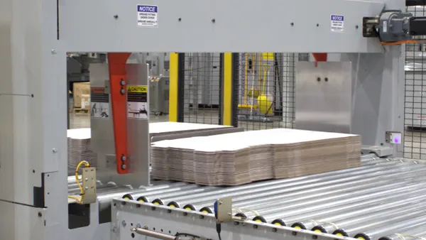 Stacks of flattened pizza boxes move across a production line in a manufacturing facility.