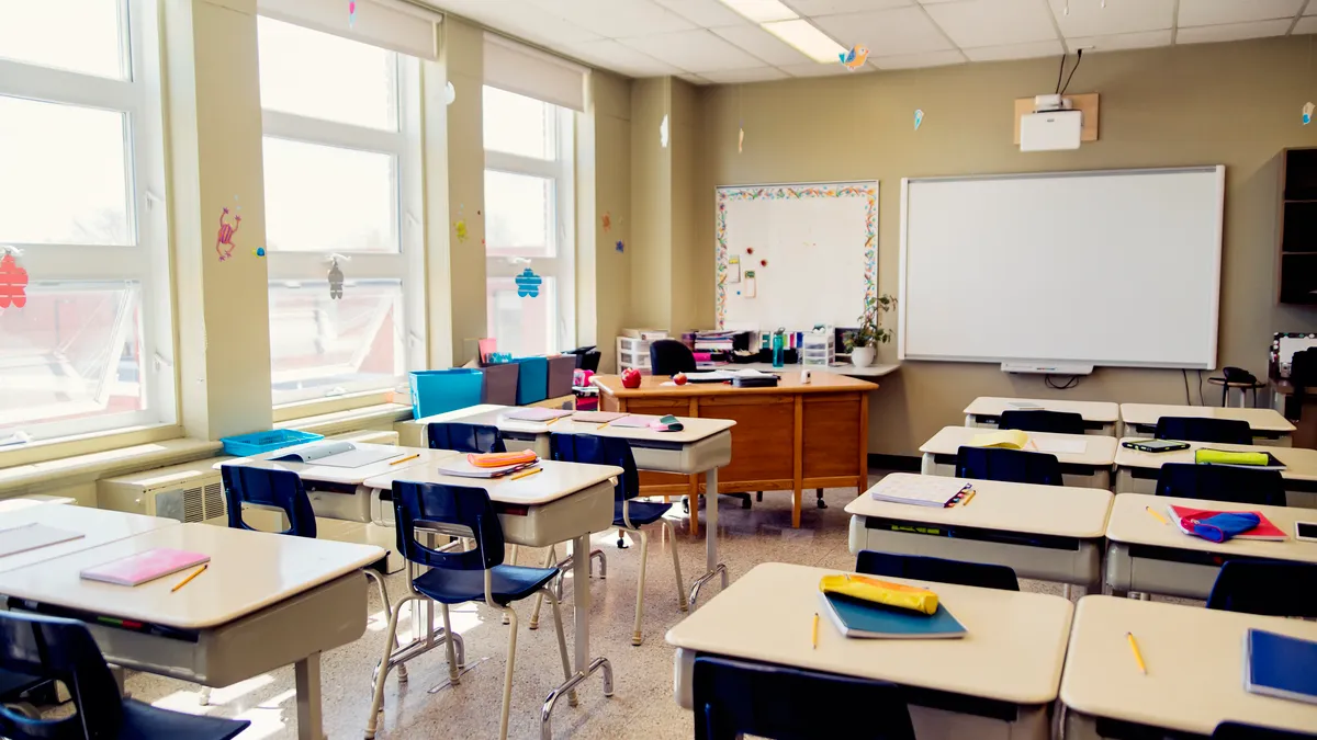 An empty elementary classroom which includes an interactive whiteboard at the side of teacher’s desk.