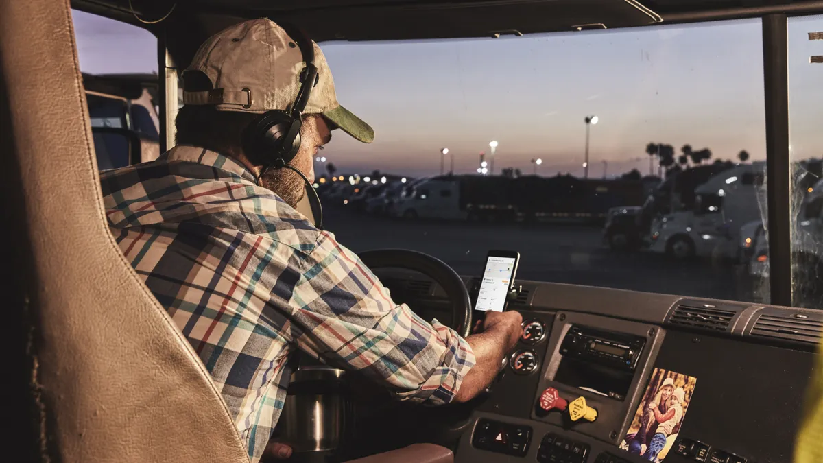 An Uber Freight driver sits in the cab of a truck using a cell phone app.