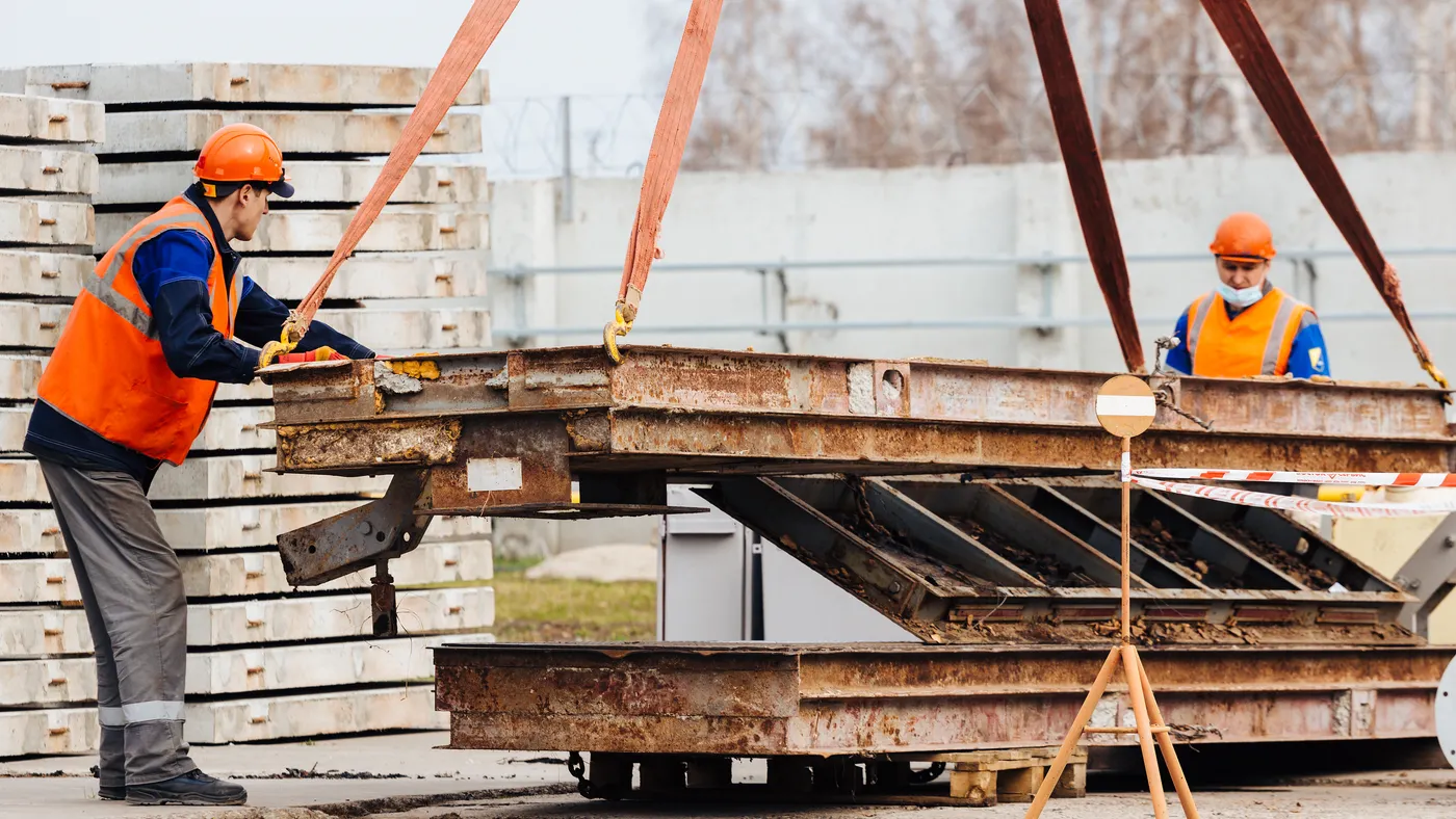 Slinger in helmet and vest controls unloading of metal structures on construction site.