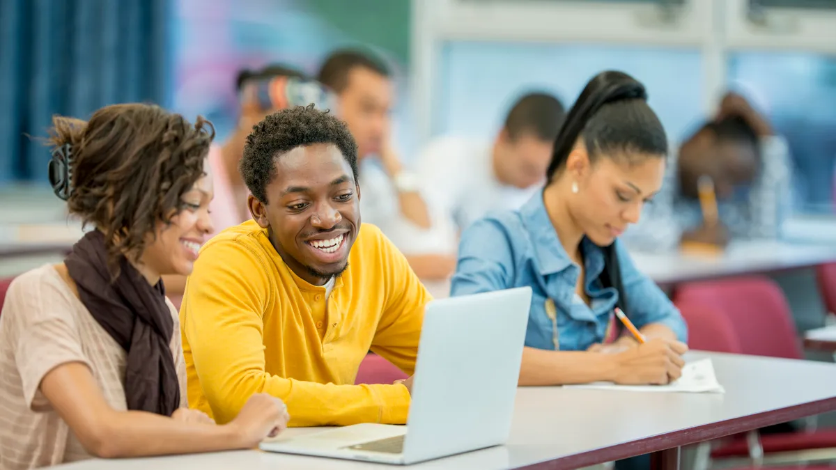 Three Black young adults take notes during a college class.