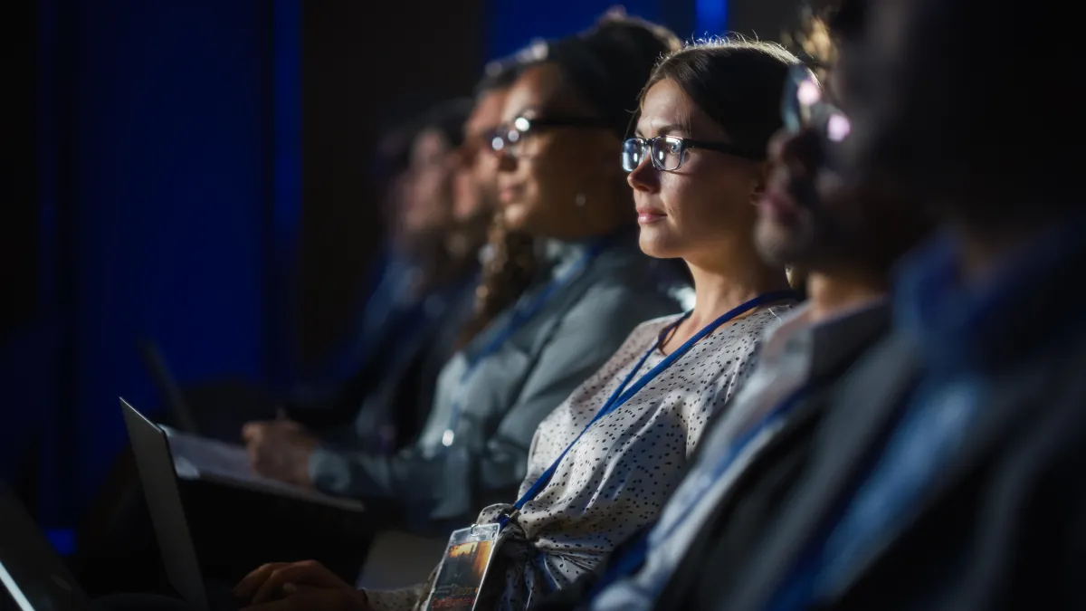 A group of people sit in a row listening to a speaker.