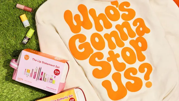 A cream colored hoodies that says "Who's Gonna Stop Us?" next tow two beauty kit boxes on grass